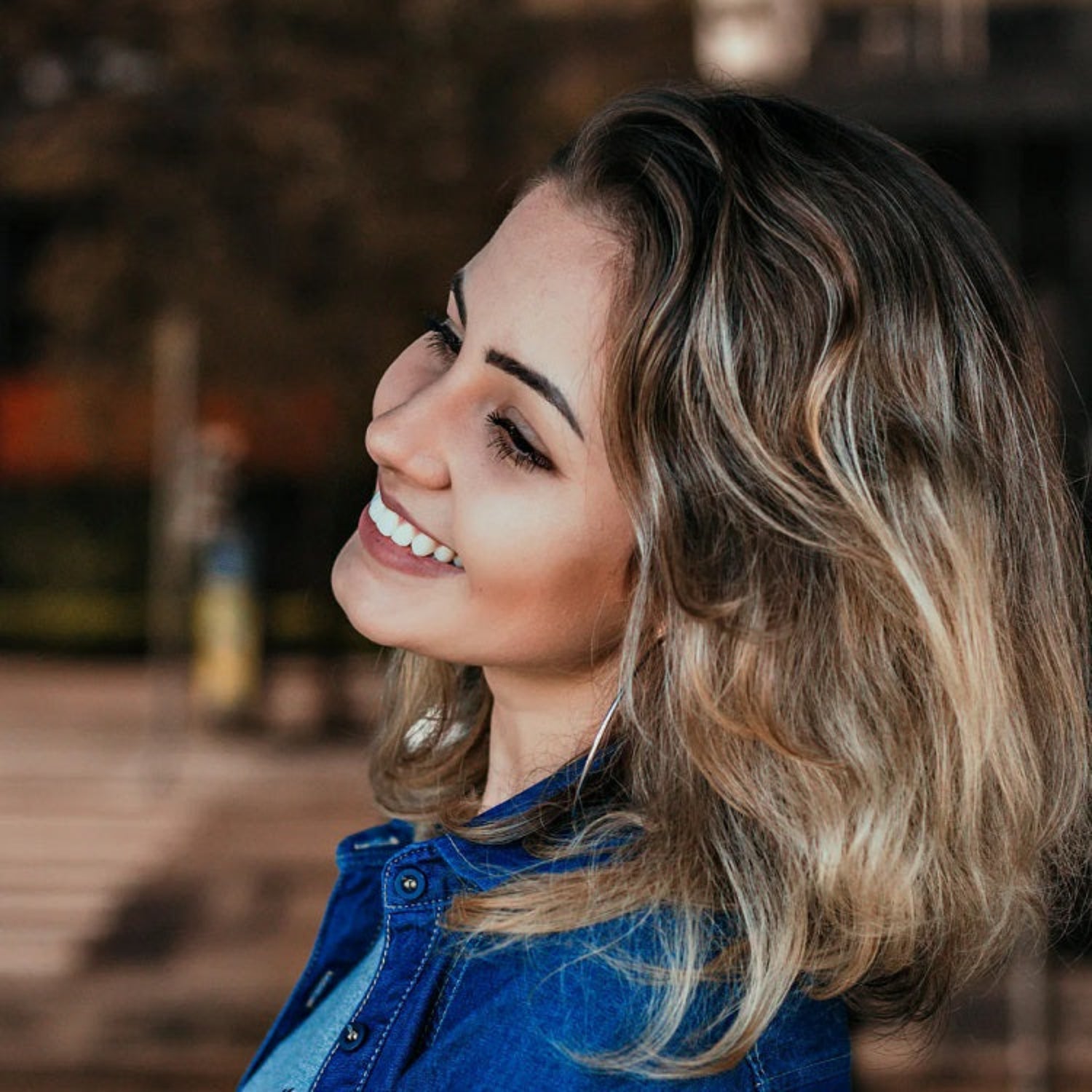 Woman with blonde hair and blue denim jacket smiling outdoors