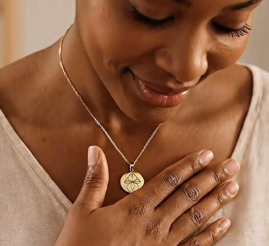Woman wearing a gold Embrella necklace with a pendant, touching her chest. Symbolizing infertility, miscarriage and loss.